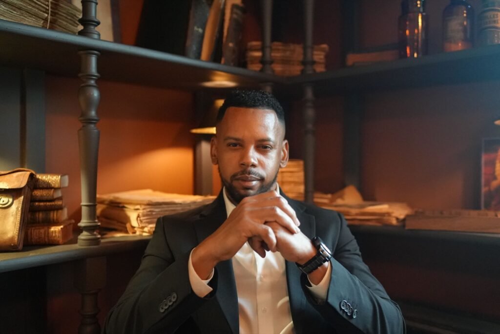 Naxice Said Salim en costume, assis dans une bibliotheque